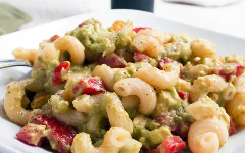 Ein cremiger nudelsalat mit avocado, Tomaten und Gewürzen auf einem weißen Teller.