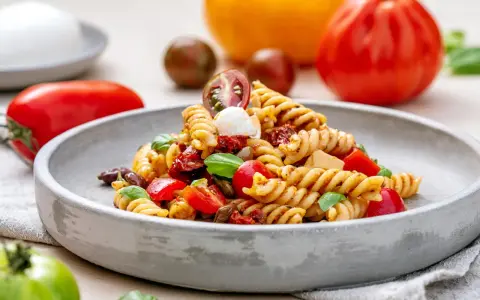 Ein köstlicher nudelsalat mit essig, garniert mit frischem Basilikum, Kirschtomaten und Mozzarella-Kugeln.
