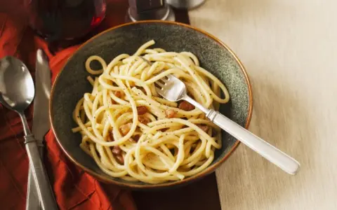 Eine Schüssel Spaghetti mit Speck und Pfeffer, eine köstliche Carbonara ohne Ei, serviert mit einem Glas Rotwein.