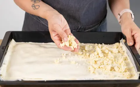 Hände verteilen Streusel auf einem Teigboden für ein Prasselkuchen Rezept DDR.