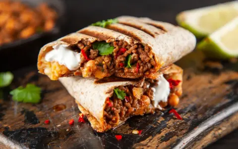 Zwei saftige Burritos, gefüllt mit Hackfleisch, Bohnen und einem Klecks Sauerrahm, sind ein köstliches burrito rezept. Garniert mit Koriander und Chili.