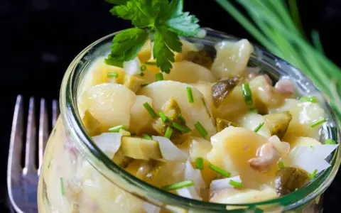 Ein köstlicher Kartoffelsalat ohne Mayo, mit Gurken, Zwiebeln und frischen Kräutern, serviert in einem Glas.
