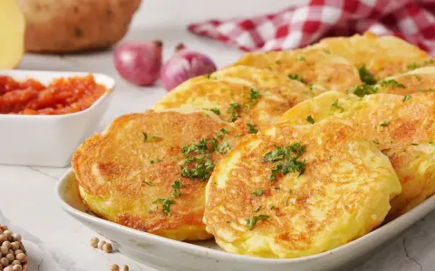 Goldbraune Kartoffelpuffer, garniert mit Petersilie, sind ein köstliches Beispiel für Rezepte mit Kartoffeln als Hauptspeise. Dazu passen Tomatensoße und Zwiebeln.