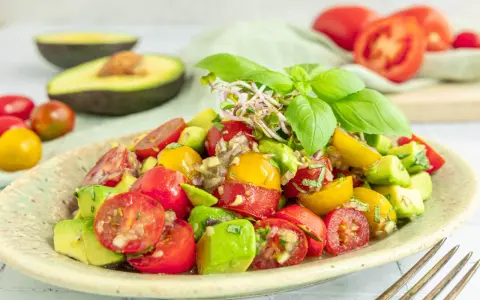 Frischer Avocado Tomaten Salat mit Basilikum und Sprossen, garniert mit roten und gelben Kirschtomaten.