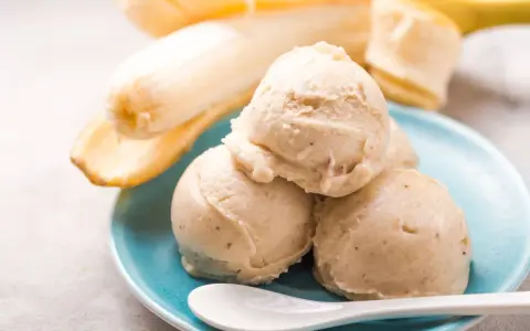 Cremiges Bananeneis, ganz einfach eis selber machen ohne eismaschine. Dazu reife Bananen und eine weiße Löffel auf blauem Teller.