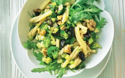 Frischer nudelsalat mit brokkoli, Walnüssen, Oliven und Rucola in einer weißen Schüssel.