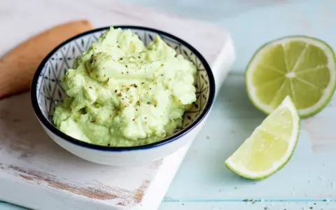 Cremiger Avocado Feta Dip, gewürzt mit Pfeffer, daneben frische Limettenspalten. Perfekt zum Dippen!
