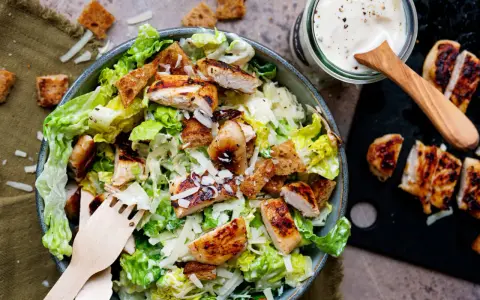 Frischer Caesar Salat mit gegrilltem Hähnchen, Croutons und Parmesan. Dazu ein Glas mit cremigem Caesar Salat Dressing.