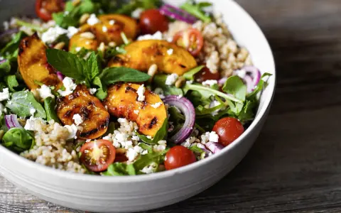 Ein bunter Pfirsich Feta Salat mit gegrillten Pfirsichspalten, Kirschtomaten, Rucola und Getreide.