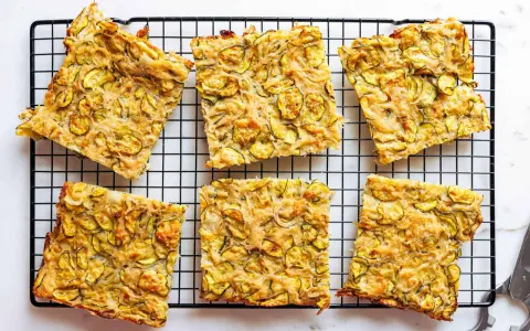 Sechs rechteckige Stücke Zucchini Scarpaccia liegen auf einem schwarzen Gitterrost.