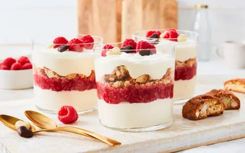 Schichtdessert mit Himbeeren, knusprigen Keksen und cremigem **dessert mit mascarpone**, garniert mit frischen Beeren und Schokolade.