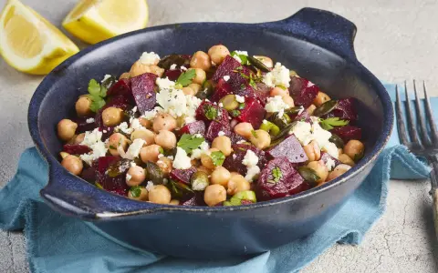 Ein bunter rote Bete Kichererbsen Salat mit Feta und Kürbiskernen in einer blauen Schüssel, garniert mit Petersilie und Zitronenspalten.