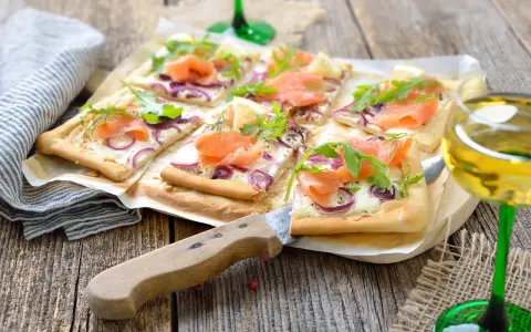 Flammkuchen mit Lachs und Crème fraîche, garniert mit Rucola und Dill, auf rustikalem Holztisch.