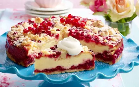 Saftiger Johannisbeerkuchen mit Quark und Streuseln, garniert mit frischen roten Johannisbeeren und einem Klecks Sahne.
