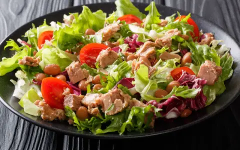 Frischer Thunfischsalat mit knackigem Salat, Tomaten und Bohnen auf schwarzem Teller.