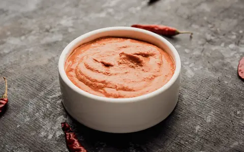 Eine Schale mit cremiger Piri Piri Sauce, umgeben von getrockneten Chilis auf dunklem Untergrund.