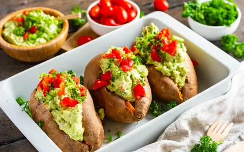 Gefüllte Süßkartoffeln mit Avocado-Topping. Leckere, kalte Rezepte mit Avocado, garniert mit Paprika und Kräutern.