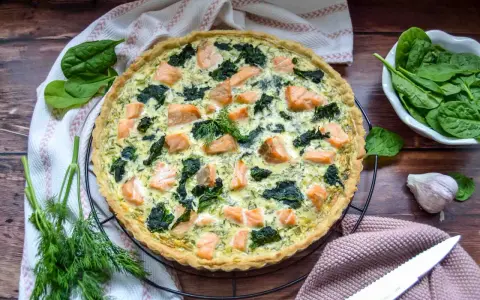 Herzhafte Spinat Lachs Quiche mit frischem Dill garniert, bereit zum Servieren.