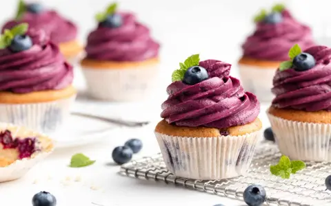 Mehrere Muffins mit lila Beeren-Topping, garniert mit frischen Blaubeeren und Minze. Ein einfacher, köstlicher Genuss.