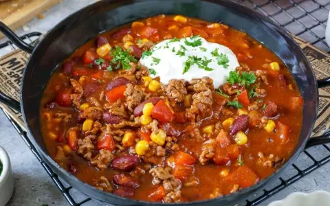 Herzhaftes Chili con Carne mit Hackfleisch, Kidneybohnen, Mais und Paprika, garniert mit einem Klecks Sauerrahm und Petersilie.