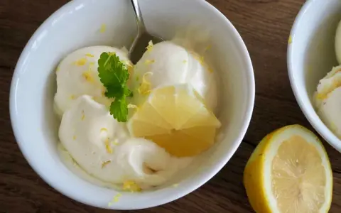 Erfrischendes zitroneneis selber machen: Cremiges Eis in einer Schüssel, garniert mit Zitronenspalte und Minze.