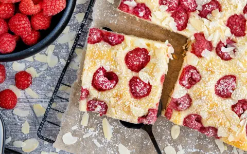 Schneller Kuchen mit gefrorenen Himbeeren, bestreut mit Puderzucker und Mandelblättchen. Ein Genuss für jeden Anlass!