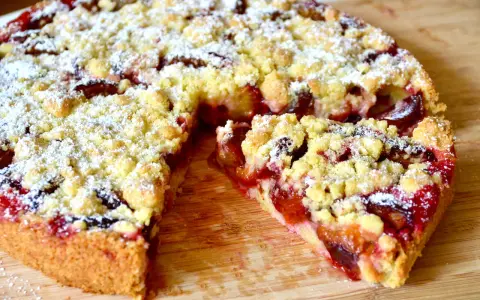 Saftiger pflaumenkuchen ohne hefe springform, mit Streuseln und Puderzucker bestäubt, auf einem Holzbrett.