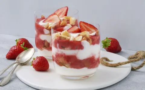 Zwei Gläser mit einem sommerlichen Dessert aus Erdbeeren und Sahne, garniert mit frischen Erdbeeren und Keksen. Ein schnell und einfach zubereitetes Genusserlebnis.