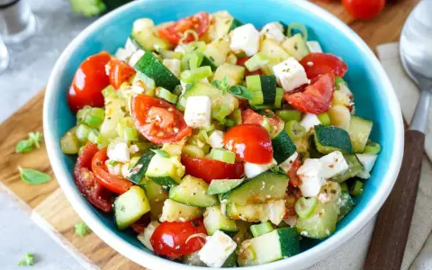 Erfrischender Zucchini Salat mit Tomaten, Feta und Frühlingszwiebeln, garniert mit frischen Kräutern. Ein leichter Genuss.