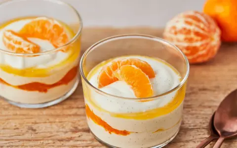 Zwei Gläser mit cremiger Quarkspeise mit Mandarinen, garniert mit frischen Mandarinenspalten.