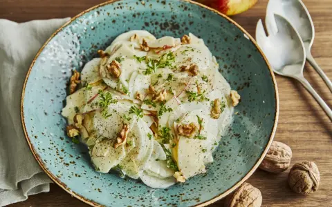 Ein erfrischender rettichsalat mit apfel, garniert mit Walnüssen und Petersilie, auf einem türkisfarbenen Teller.