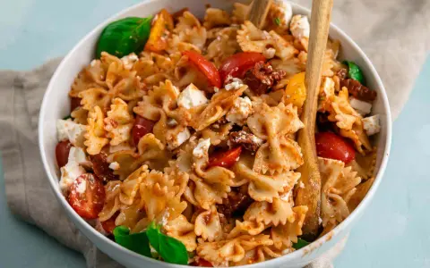 Ein köstlicher Nudelsalat mit Farfalle, frischen Tomaten, Mozzarella und sonnengetrockneten Tomaten, garniert mit Basilikum.