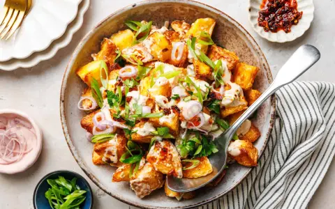 Kartoffelsalat mal anders: knusprige Kartoffelspalten mit cremiger Sauce, Frühlingszwiebeln und roten Zwiebelringen in einer rustikalen Schüssel.