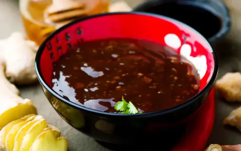 Schwarze Schüssel mit glänzender Teriyaki-Sauce, umgeben von Ingwer, Knoblauch und Chili. Ein köstliches teriyaki sauce rezept zum Nachkochen.