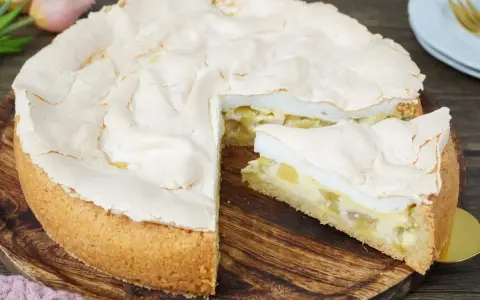 Ein saftiger Rhabarberkuchen mit luftigem Baiser, ein Stück davon ist bereits angeschnitten.