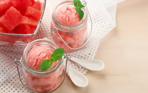 Erfrischendes Meloneneis selber machen: Rosa Sorbet in Gläsern mit Minze, daneben eine Schale mit Wassermelonenwürfeln.