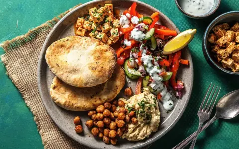 Ein bunter griechischer Salat mit Hummus, gerösteten Kichererbsen und Pitabrot. Dazu gewürfelter Tofu und ein Zitronenschnitz.