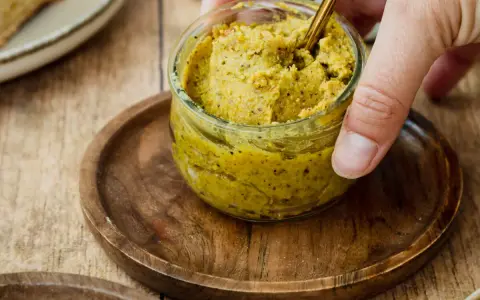 Ein Glas mit selbstgemachter Pistaziencreme, die mit einem goldenen Löffel umgerührt wird. Perfekt zum Brot oder als Dip.