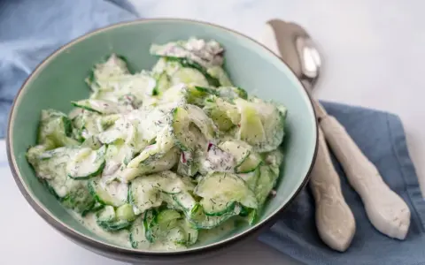 Frischer gurkensalat mit saurer sahne, garniert mit Dill und roten Zwiebeln, serviert in einer hellgrünen Schüssel.