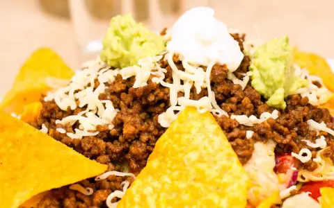 Schichtsalat mit Hackfleisch, Käse, Guacamole und saurer Sahne, garniert mit knusprigen Nachos.