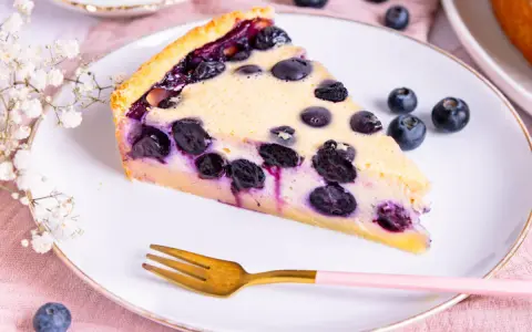 Ein Stück Blaubeerkuchen auf einem Teller, inspiriert von Landfrauen Kuchen Rezepten. Mit frischen Blaubeeren und zarter Füllung.