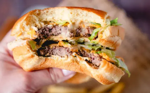 Ein saftiger Burger mit zwei Rindfleisch-Patties, Salat und der unverwechselbaren Big Mac Sauce, gehalten in einer Hand.