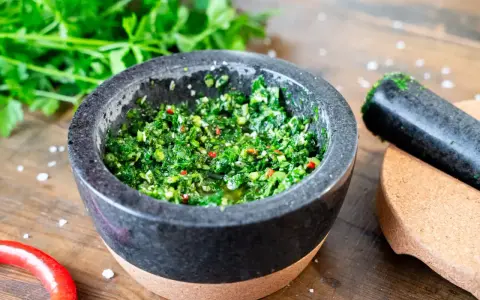 Frisches Chimichurri-Rezept im Mörser, bereit zum Verfeinern von Grillgut. Kräuter, Chili und Gewürze sind fein gehackt.