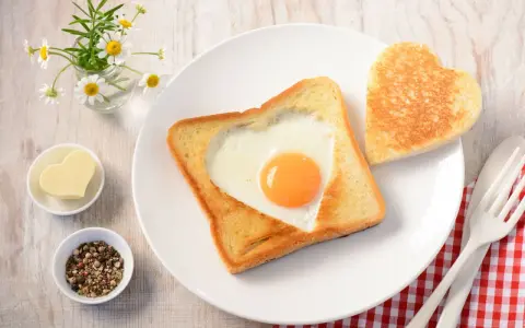Herzförmiger Toast mit Ei, daneben ein Herzbutterstück und ein Herz-Toast. Ein liebevolles Frühstück.