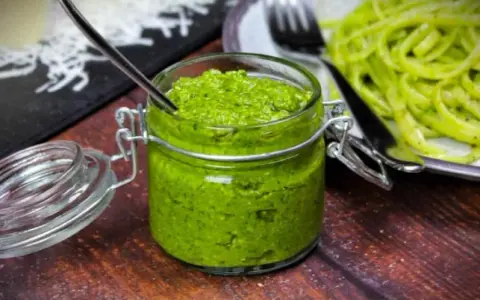 Frisches Rucola Pesto in einem Glas mit Löffel, daneben Pasta.