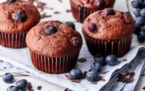 Saftige schoko blaubeer muffins, garniert mit frischen Blaubeeren und Schokostückchen, liegen auf einem Leinentuch.