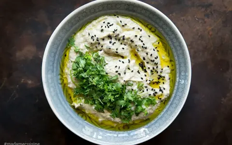 Cremiges Baba Ganoush, beträufelt mit Olivenöl, garniert mit frischer Petersilie und schwarzen Sesamkörnern.