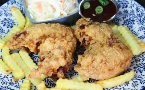 Knusprige chicken wings mit Pommes, Cole Slaw und BBQ-Sauce auf einem blau-weißen Teller.