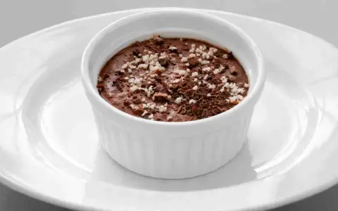 Ein cremiges Mousse au Chocolat, garniert mit Schokoladenraspeln und feinen Salzkristallen, serviert in einer weißen Schale auf einem Teller.