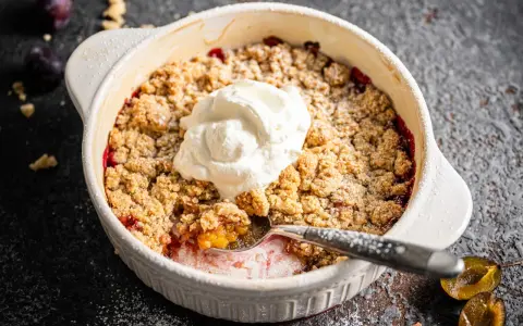 Ein köstlicher Zwetschgen Crumble mit Haferflocken, gekrönt mit einem Klecks Sahne, wartet darauf, genossen zu werden.